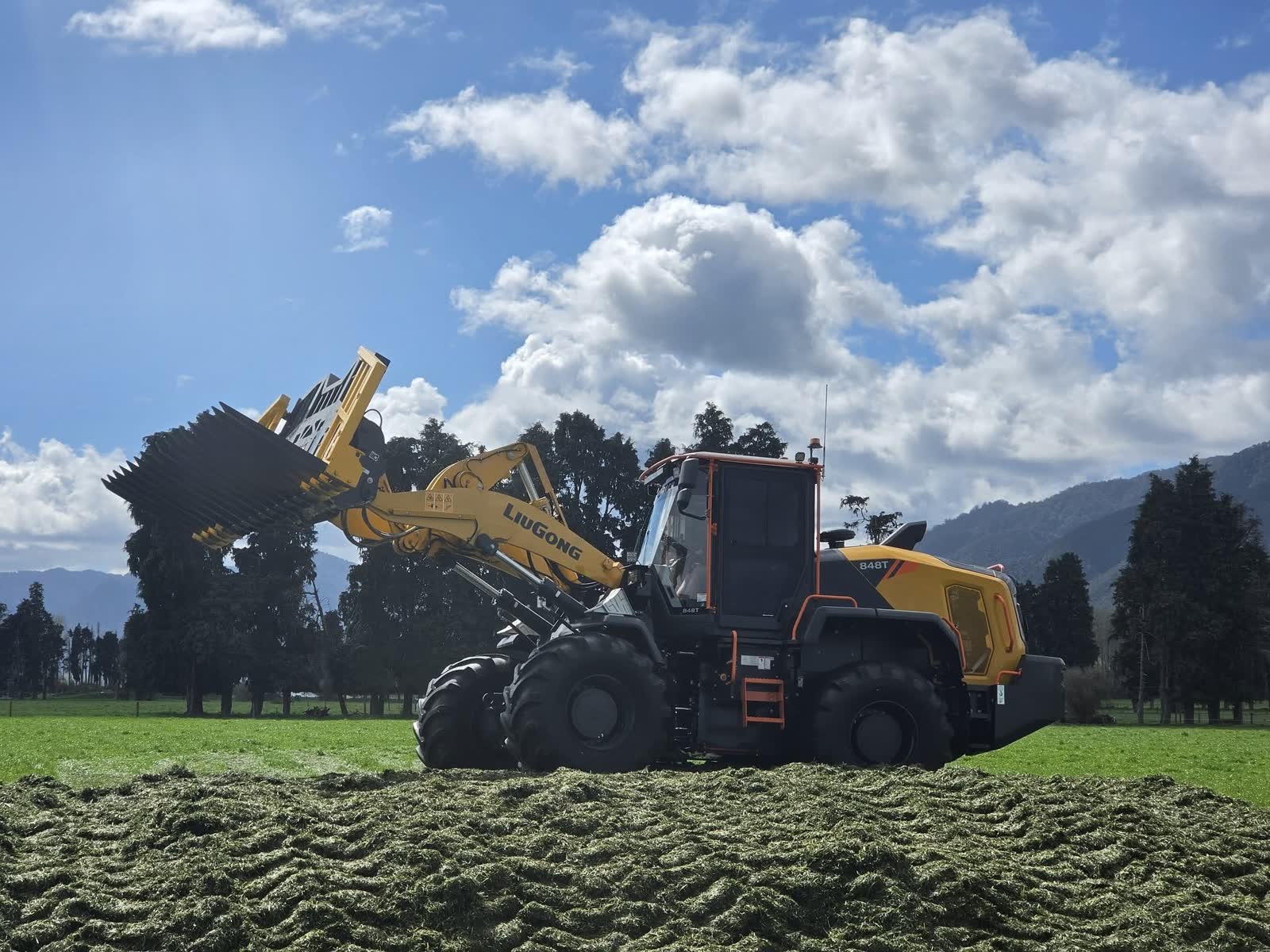 Yellow loader beside a trailer in a field with cut grass.