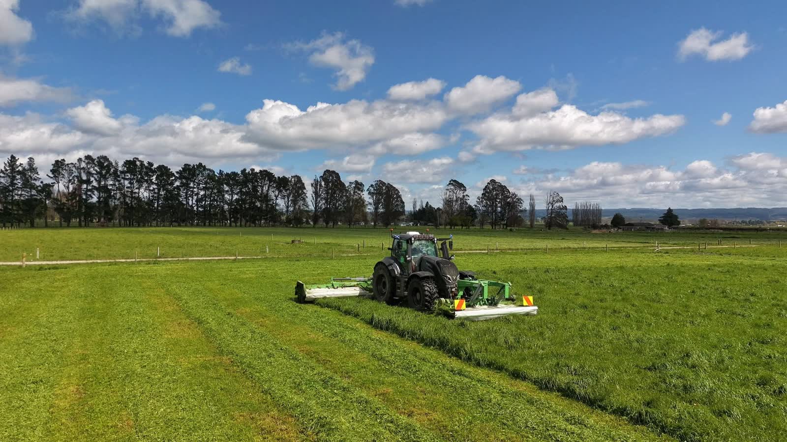 Tractor and wide implement working across a green field under a cloudy sky.